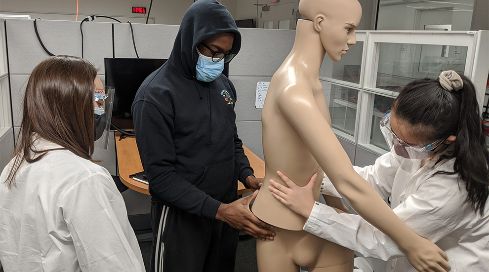 students in lab coats working with a mannequin